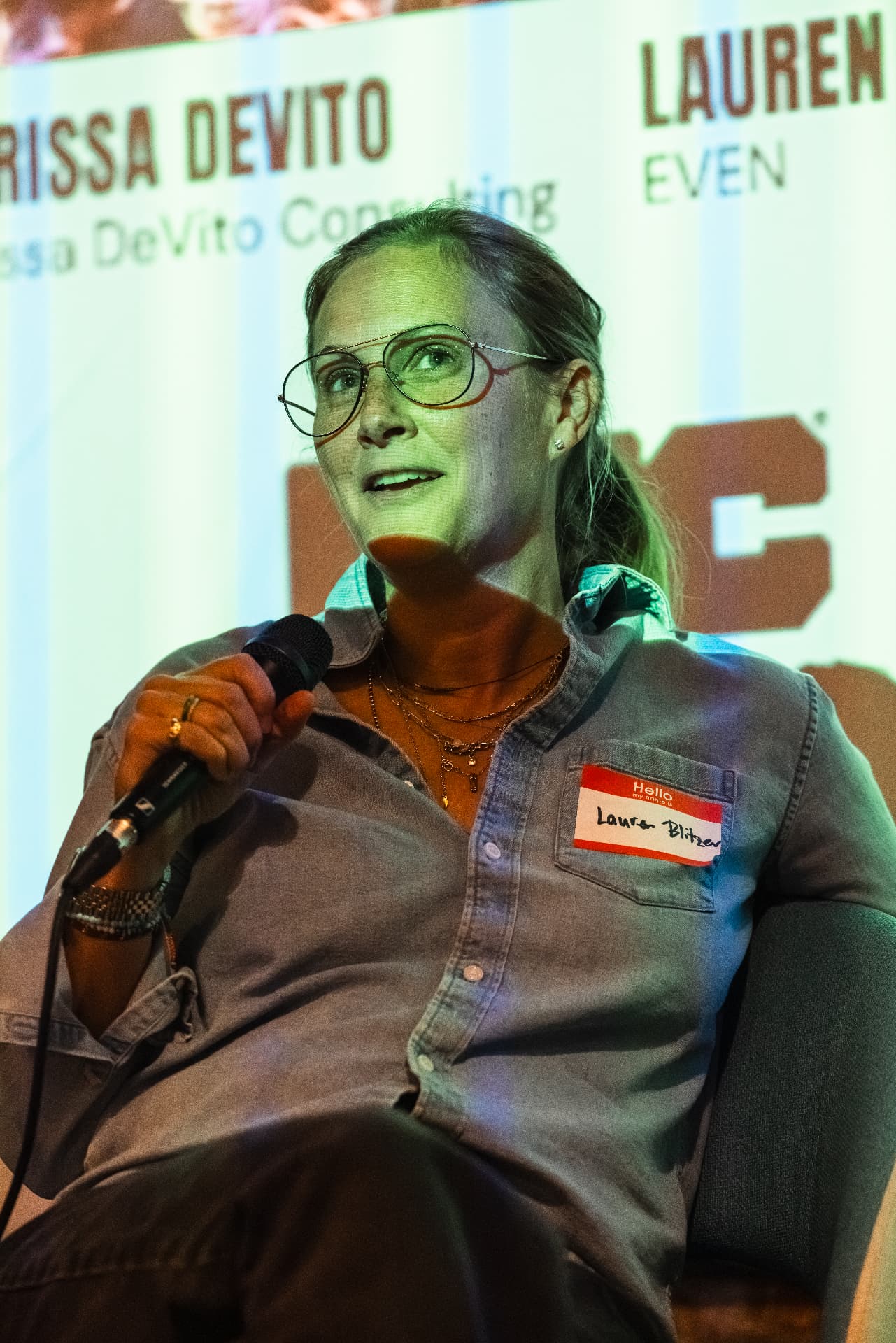 Lauren Blitzer speaking into a microphone while seated on stage at a Lone Wolves Community event